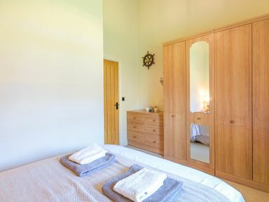 A bedroom with a bed, wooden wardrobe, dresser, and a door at Lavender Cottage Village Farm in Seahouses