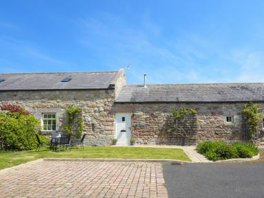 A stone cottage with a white door and outdoor seating on a lawn at Lavender Cottage Village Farm in Seahouses