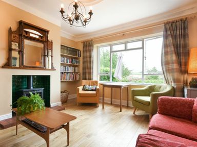 A living room with a green armchair a red sofa and a wooden table with a plant at Estuary View in Alnmouth
