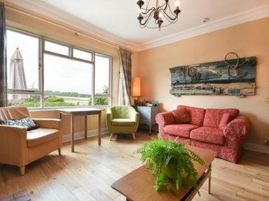 A living room with a red sofa green and beige armchairs a wooden coffee table with a plant and a decorative wall piece at Estuary View in Alnmouth