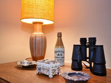 A table with a lamp a bottle a pair of binoculars and decorative items at Estuary View in Alnmouth