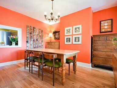 A dining room with wooden table and chairs orange walls and wooden dressers with framed art at Estuary View in Alnmouth