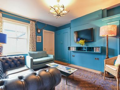 A living room with blue walls a television on the wall and sofas at Estuary View in Alnmouth