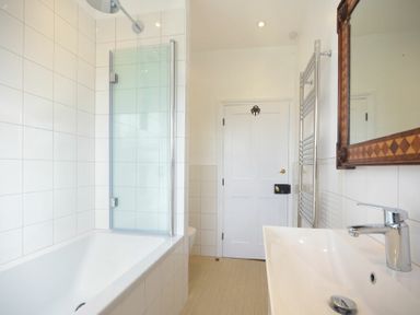 A bathroom with a bathtub shower combination a white sink a mirror and a towel rack at Estuary View in Alnmouth