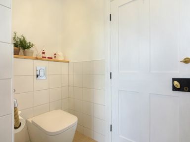 A small bathroom with a wall-mounted toilet plants and decorative items on a shelf at Estuary View in Alnmouth