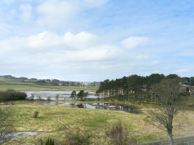 A landscape with fields trees water and a house in the distance at Estuary View in Alnmouth