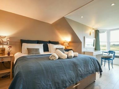 A bedroom with a large bed and blue bedding next to a window with countryside view at Estuary View in Alnmouth