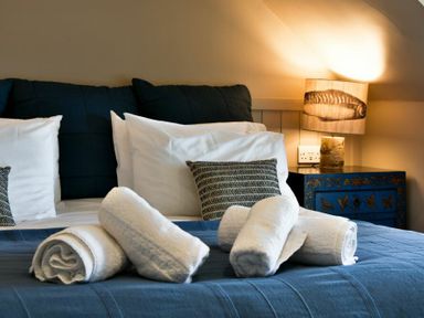 A bedroom with a bed with white pillows and rolled towels on a blue bedspread and a bedside table with a lamp at Estuary View in Alnmouth