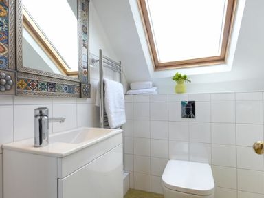 A bathroom with a sink, mirror, towel rack, toilet, skylight, and folded towels at Estuary View in Alnmouth