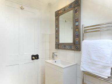 A bathroom with a sink and faucet a decorative mirror a towel rack with a white towel and a white door at Estuary View in Alnmouth