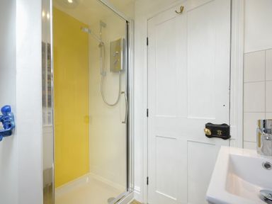 A bathroom with a shower enclosure with a yellow wall panel a white door and a sink at Estuary View in Alnmouth