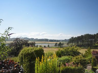 A garden with various plants and shrubs overlooking fields a river and trees at Estuary View in Alnmouth