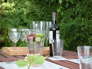 A wooden outdoor table with a water jug containing cucumber slices and a bottle of wine with empty glasses at Estuary View in Alnmouth