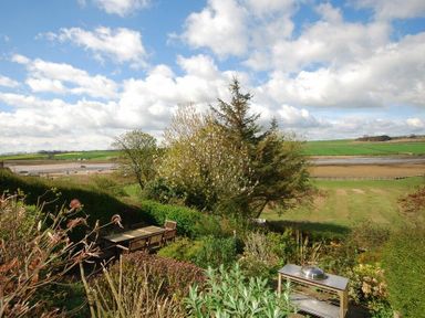 A garden with outdoor table and chairs overlooking a river and green fields at Estuary View in Alnmouth