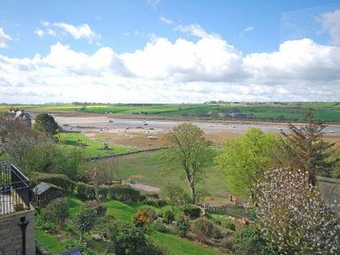 A garden with trees and bushes overlooking a river estuary with boats on the water at Estuary View in Alnmouth