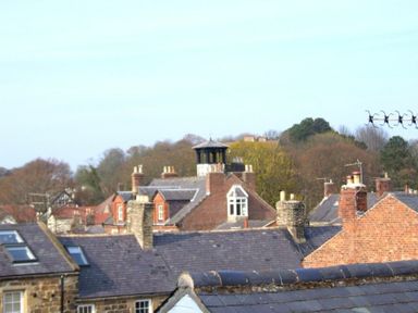 A view of rooftops with chimneys and trees in the background at Estuary View in Alnmouth