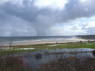 A beach with waves and wetlands under a cloudy sky at Estuary View in Alnmouth