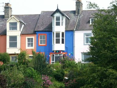 A row of houses with colorful facades and a garden with bushes and flowers in front at Estuary View in Alnmouth