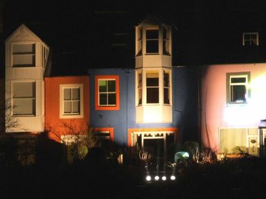 A row of houses at night with colored facades including white blue orange and pink at Estuary View in Alnmouth