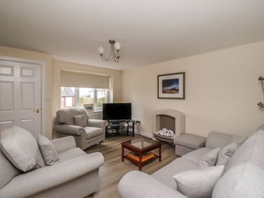 A living room with grey sofas a TV on a stand a small glass coffee table and a fireplace at Sandy Shores in Seahouses