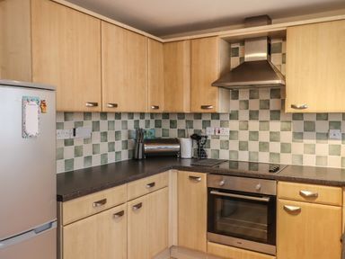 A kitchen with wooden cabinets a stainless steel oven a stovetop a silver refrigerator and a tiled backsplash at Sandy Shores in Seahouses