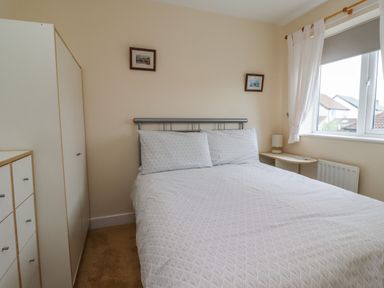 A bedroom with a double bed, wardrobe, chest of drawers, nightstand, lamp, and window at Sandy Shores in Seahouses