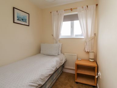 A small bedroom with a single bed next to a window and a wooden bedside table with a lamp Sandy Shores Seahouses