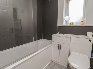 A bathroom with a bathtub, sink, cabinet, toilet, and a window at Sandy Shores in Seahouses