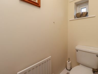 A small bathroom with a toilet a toilet paper holder radiator and a small window with a metallic bowl on the sill at Sandy Shores in Seahouses