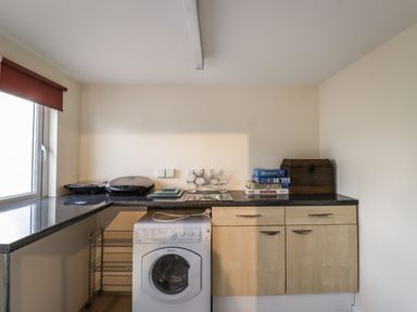 A utility room with a washing machine under a black countertop with game boxes and a chest on top at Sandy Shores in Seahouses