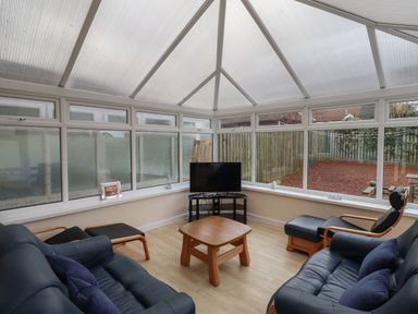 A conservatory with leather sofas a wooden coffee table and a TV at Sandy Shores in Seahouses