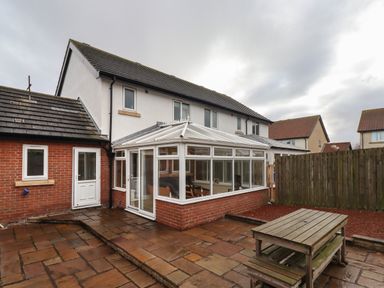 A back patio with a wooden picnic table and a conservatory attached to a two-story house