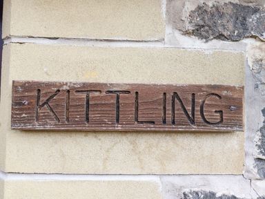 A wooden sign with the word Kittling carved into it mounted on a stone wall at Kittling Cottage in Bamburgh