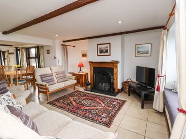 A living room with sofas a rug a fireplace a television and a dining area at Kittling Cottage in Bamburgh