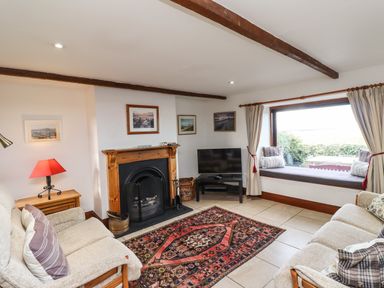 A living room with sofas a fireplace a television and a window seat at Kittling Cottage in Bamburgh