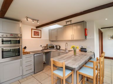 A kitchen with wooden chairs around a kitchen island and cabinets at Kittling Cottage in Bamburgh