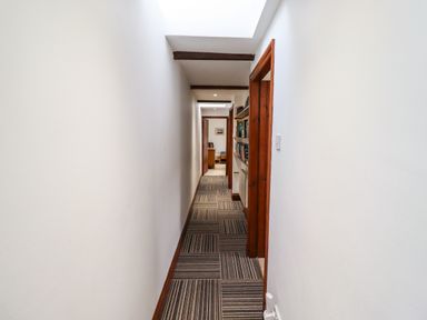 A narrow hallway with striped carpet flooring wooden door frames and a built-in bookshelf at Kittling Cottage in Bamburgh