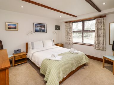 A bedroom with a double bed two bedside tables a window with curtains and a wall mirror at Kittling Cottage in Bamburgh