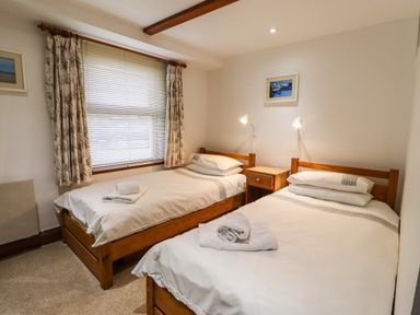 A bedroom with two single beds a wooden nightstand and window with curtains at Kittling Cottage in Bamburgh