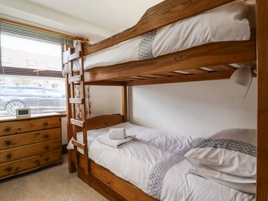 A bedroom with a wooden bunk bed and towel on the lower bed and a wooden dresser by the window at Kittling Cottage in Bamburgh