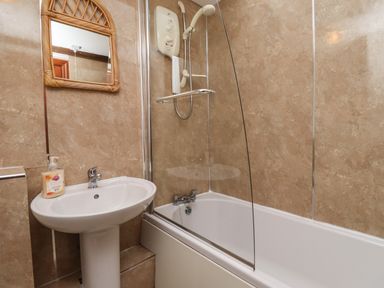 A bathroom with a pedestal sink and a bathtub with a shower screen at Kittling Cottage in Bamburgh