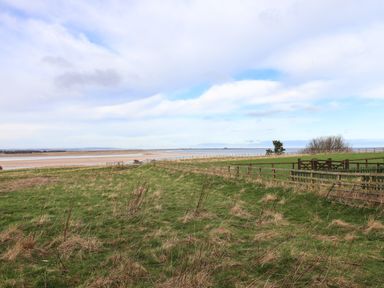 A grassy field with fences and a sandy beach in the distance at Kittling Cottage Bamburgh