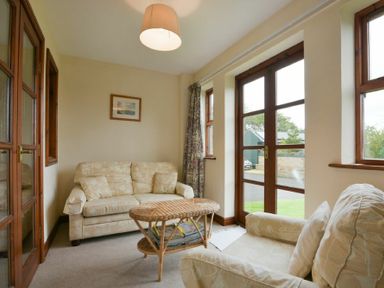A sitting room with two sofas a wicker coffee table and glass doors at Smithy Court in Craster