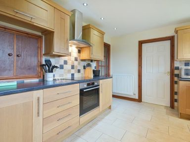 A kitchen with wooden cabinets a built in oven and a closed white door at Smithy Court in Craster
