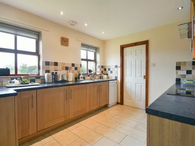 A kitchen with wooden cabinets black countertops tiled floor and a white door at Smithy Court in Craster