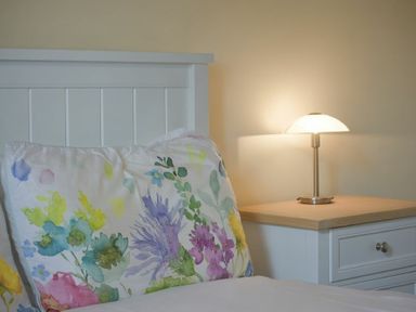 A bed with floral patterned pillow next to a white bedside table with a lamp at Smithy Court in Craster