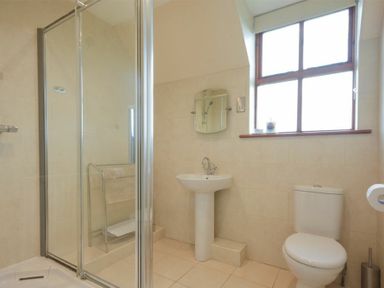 A bathroom with a shower cubicle sink and toilet and a window above the sink at Smithy Court in Craster
