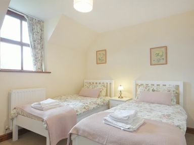 A bedroom with two single beds with floral bedding and towels on the beds at Smithy Court in Craster
