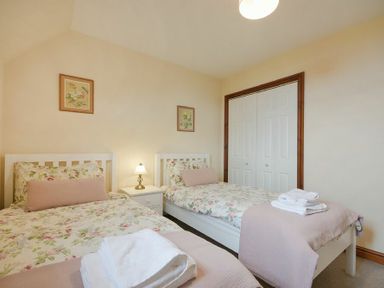 A bedroom with two single beds floral bedding bedside table lamp and a closet at Smithy Court in Craster