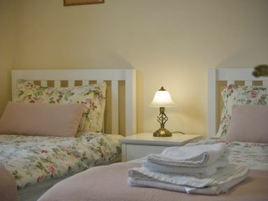 Two single beds with floral bedding and pink cushions a white bedside table with a lamp and folded towels on a bed at Smithy Court in Craster